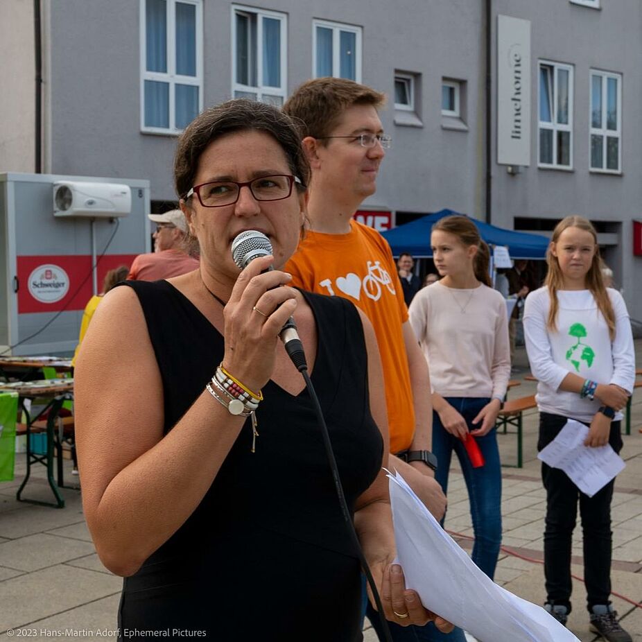 Zwei der Organisator:innen vom Bund Naturschutz (Simone Schmidt, mit Mikrofon) und ADFC (Leonard Burtscher, dahinter) begrüßten das Publikum. Zwei der Organisator:innen vom Bund Naturschutz (Simone Schmidt, mit Mikrofon) und ADFC (Leonard Burtscher, dahinter) begrüßten das Publikum.